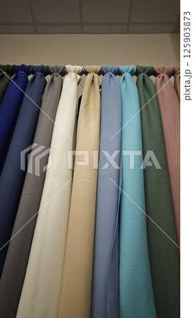 Assorted solid-colored fabrics hanging vertically in a row with soft lighting from above. Concept of textile selection, material quality and interior or fashion design resource 125903873
