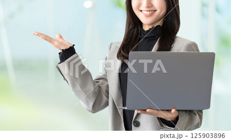 ノートパソコンを持って案内をする笑顔の女性・ビジネスウーマン ノートパソコンを持って案内をする笑顔の女性・ビジネスウーマン 125903896
