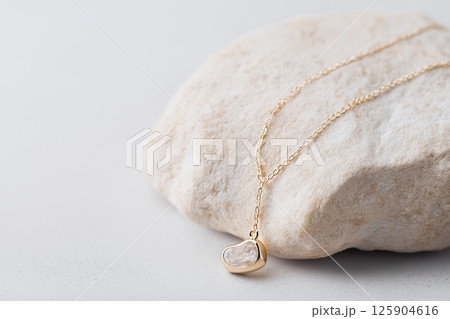 A delicate gold necklace with a polished gemstone pendant, showcased on a textured stone background. This luxury jewelry, perfect for fashion, showcasing minimalism and sophistication A delicate gold necklace with a polished gemstone pendant, showcased on a textured stone background. This luxury jewelry, perfect for fashion, showcasing minimalism and sophistication 125904616