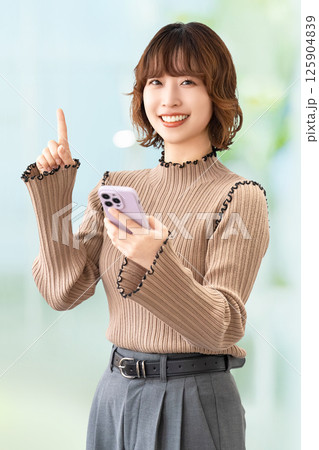 スマートフォンを持って案内をする笑顔の女性・ビジネスウーマン スマートフォンを持って案内をする笑顔の女性・ビジネスウーマン 125904839