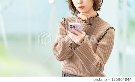 スマートフォンを見て考える女性・ビジネスウーマン スマートフォンを見て考える女性・ビジネスウーマン 125904844