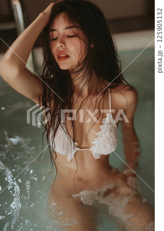 Young woman in a bathtub with wet hair, featuring a serene and captivating expression. The composition exudes calmness, highlighting her natural beauty and the soothing atmosphere of the bathing. 125905132