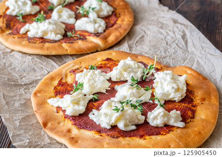 Mini pizzas baked with tomato sauce, stracciatella cheese, and fresh thyme garnish Mini pizzas baked with tomato sauce, stracciatella cheese, and fresh thyme garnish 125905450