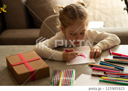 Cute 4-year-old blonde girl concentrates while drawing sitting at table. Childhood creativity, early education concept with colorful art supplies. Cute 4-year-old blonde girl concentrates while drawing sitting at table. Childhood creativity, early education concept with colorful art supplies. 125905825