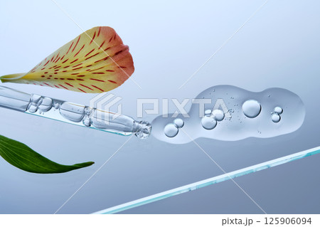 A pipette with a beautiful drop of serum on a background of lily flowers. A pipette with a beautiful drop of serum on a background of lily flowers. 125906094