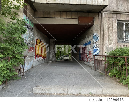 arch between old houses with graffiti, white car in the background 125906384