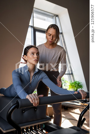 Woman doing Swan exercise on Pilates Reformer for the chest and back muscles, focusing on flexibility, strength, and control with determination 125906577