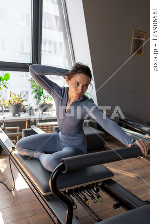 Woman doing mermaid exercise in a sunlite, modern pilates studio, embodying calm, focus, and strength. Woman doing mermaid exercise in a sunlite, modern pilates studio, embodying calm, focus, and strength. 125906581