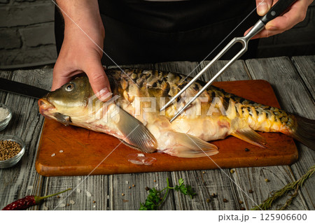 Hands skillfully prepare a fresh fish on a wooden cutting board, surrounded by herbs and spices in a rustic kitchen setting, creating an inviting culinary atmosphere 125906600