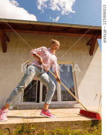 Woman cleaning patio using brush broom 125906813