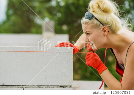 Woman using string as level in wall construction. Woman using string as level in wall construction. 125907051
