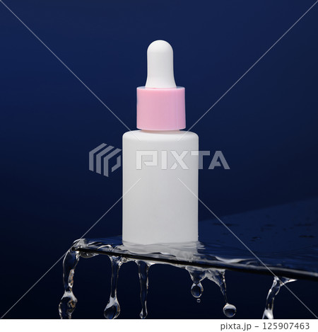 In the blue background, a bottle of serum stands on glass. Drops of water drip off the glass. Promotional photo of cosmetics. Mockup. Template.  In the blue background, a bottle of serum stands on glass. Drops of water drip off the glass. Promotional photo of cosmetics. Mockup. Template.  125907463