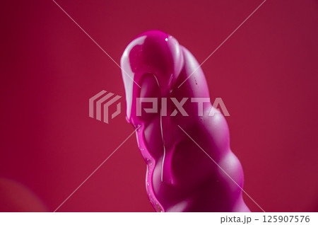 Lube pouring on pink dildo on pink background.  125907576