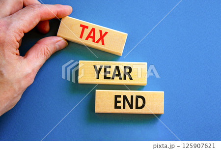 Tax year end symbol. Concept words Tax year end on beautiful wooden blocks. Beautiful blue background. Businessman hand. Business tax year end concept. Copy space. 125907621