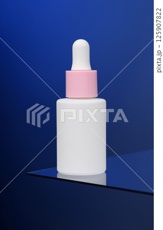 In the blue background, a bottle of serum stands on glass.  Vertical advertising photo of cosmetics. Mockup. Template.  125907822