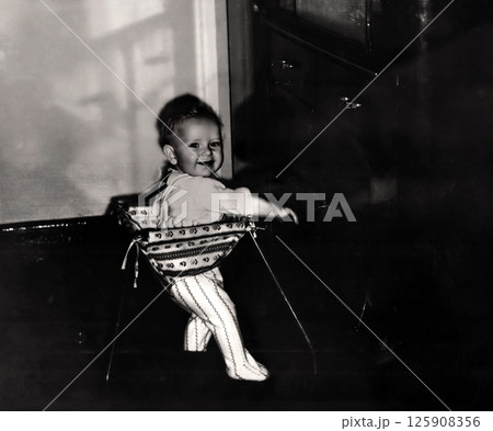 Vintage portrait of little boy in a walker. The child learns to walk. Retro photo 1967. 125908356