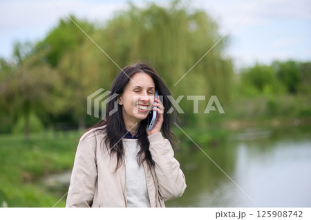 Smiling woman making a video call in park and pointing upward Smiling woman making a video call in park and pointing upward 125908742