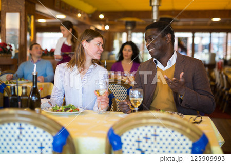 Cheerful adult biracial couple enjoying dinner in restaurant Cheerful adult biracial couple enjoying dinner in restaurant 125909993