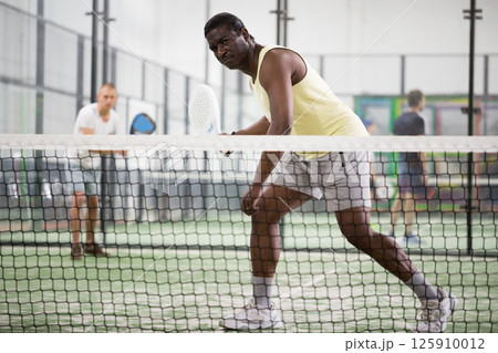 Sporty afro american man playing padel tennis indoor 125910012