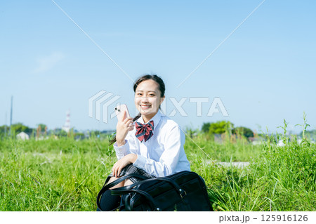 青空の下でスマホを持つ女子高校生 125916126