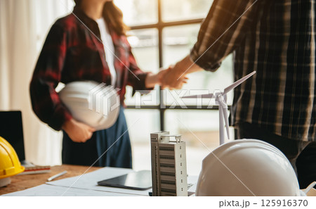Engineers or architecture shaking hands at construction site for architectural project, holding safety helmet on their hands. 125916370