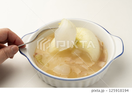 新玉ねぎの丸ごと煮込みスープの玉ねぎをフォークで持ち上げる 125918194