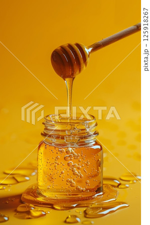 A Glass Jar with a Lid on a Solid Color Background with Honey and a Stirring Stick A Glass Jar with a Lid on a Solid Color Background with Honey and a Stirring Stick 125918267