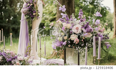 Elegant wedding dining table with candles floral arrangements in shades of purple, lavender and pink in a garden 125918406