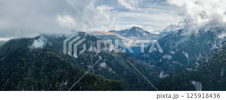 A breathtaking panorama of a mountainous landscape shrouded in mist. Lush greenery slopes into misty valleys beneath a dynamic sky, creating a serene yet dramatic view. Panorama of mountain range 125918436