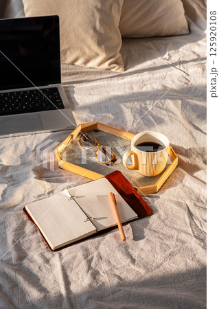 Laptop, Notebook, Coffee Cup, Pen and Eyeglasses are Arranged on Bed. Freelance, Work from Home or Studying Concept. 125920108
