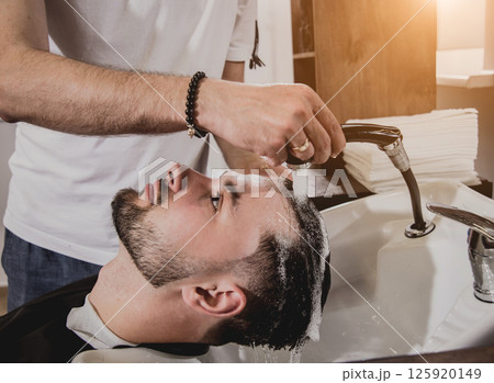 Young man with trendy haircut at barber shop. Barber washes customer head. Young man with trendy haircut at barber shop. Barber washes customer head. 125920149