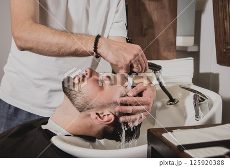 Young man with trendy haircut at barber shop. Barber washes customer head. Young man with trendy haircut at barber shop. Barber washes customer head. 125920388