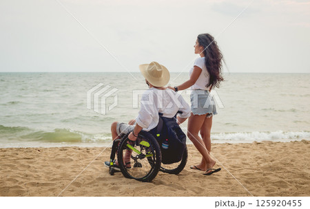 Disabled man in a wheelchair with his wife on the beach. Disabled man in a wheelchair with his wife on the beach. 125920455
