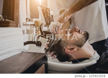Young man with trendy haircut at barber shop. Barber washes customer head. Young man with trendy haircut at barber shop. Barber washes customer head. 125921019