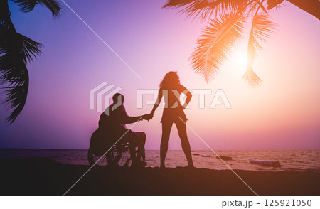 Disabled man in a wheelchair with his wife on the beach. Silhouettes at sunset 125921050