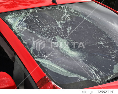 Shattered and broken windshield on a bright red car showcasing the damage to its glass surface Shattered and broken windshield on a bright red car showcasing the damage to its glass surface 125921141