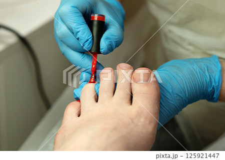 Nail technician painting outer toenail with red polish during pedicure. 125921447