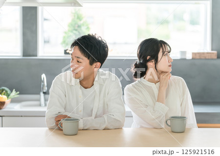 ダイニングに座る冷めた表情の若い夫婦・カップル（夫婦関係・倦怠期・マンネリ・仮面夫婦・夫婦喧嘩） 125921516