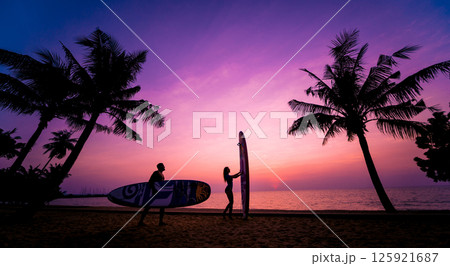 Silhouette of surfers couple holding long surf boards at sunset  125921687