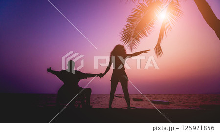 Disabled man in a wheelchair with his wife on the beach. Silhouettes at sunset Disabled man in a wheelchair with his wife on the beach. Silhouettes at sunset 125921856