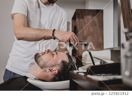 Young man with trendy haircut at barber shop. Barber washes customer head. Young man with trendy haircut at barber shop. Barber washes customer head. 125921912