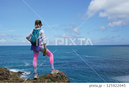 A young couple are hiking on a rugged rocky cliff that offers a view of the ocean 125922045