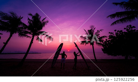 Silhouette of surfers couple holding long surf boards at sunset Silhouette of surfers couple holding long surf boards at sunset 125922256