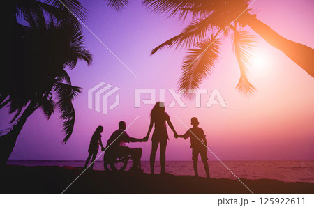Disabled man in a wheelchair with his family on the beach. Silhouettes at sunset Disabled man in a wheelchair with his family on the beach. Silhouettes at sunset 125922611