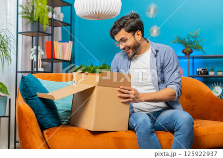 Happy Arabian man shopper unpacking cardboard box delivery parcel online shopping purchase at home Happy Arabian man shopper unpacking cardboard box delivery parcel online shopping purchase at home 125922937