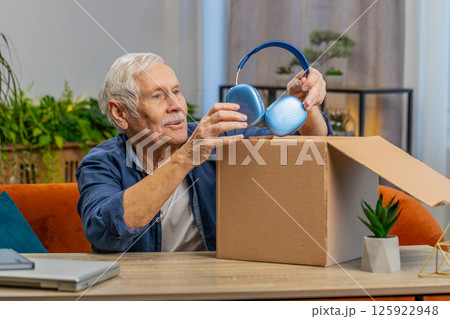 Happy senior man shopper unpacking headphones cardboard box delivery parcel online shopping purchase 125922948