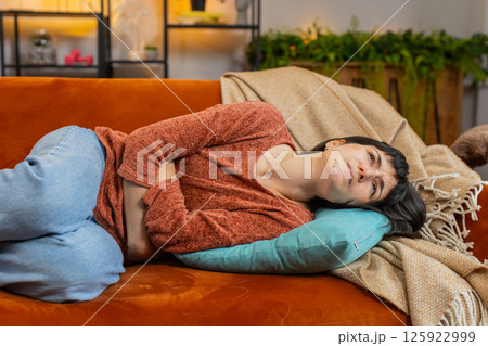 Upset woman embracing belly suffering from stomachache, menstrual painful feelings lying on couch Upset woman embracing belly suffering from stomachache, menstrual painful feelings lying on couch 125922999