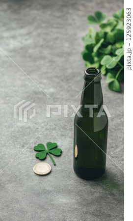 A dark green beer bottle sits on a gray surface next to a shamrock and a coin 125923063