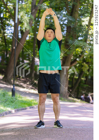 Japanese sporty healthy man athlete in park outdoors stretching hands stretch arms morning workout 125923247