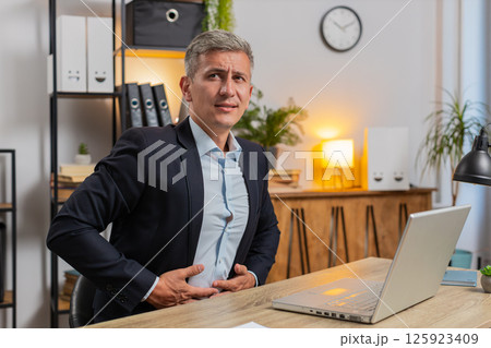 Sick young businessman in suit using laptop suddenly clutching stomach in pain at home office desk 125923409